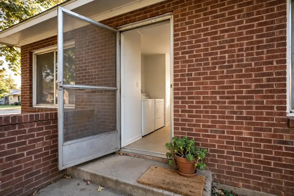 Brick bungalow entry with a screen door opening onto a washer and dryer